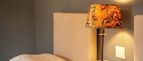 A bedside table with a lamp, a bed with a white blanket, and a nightstand.