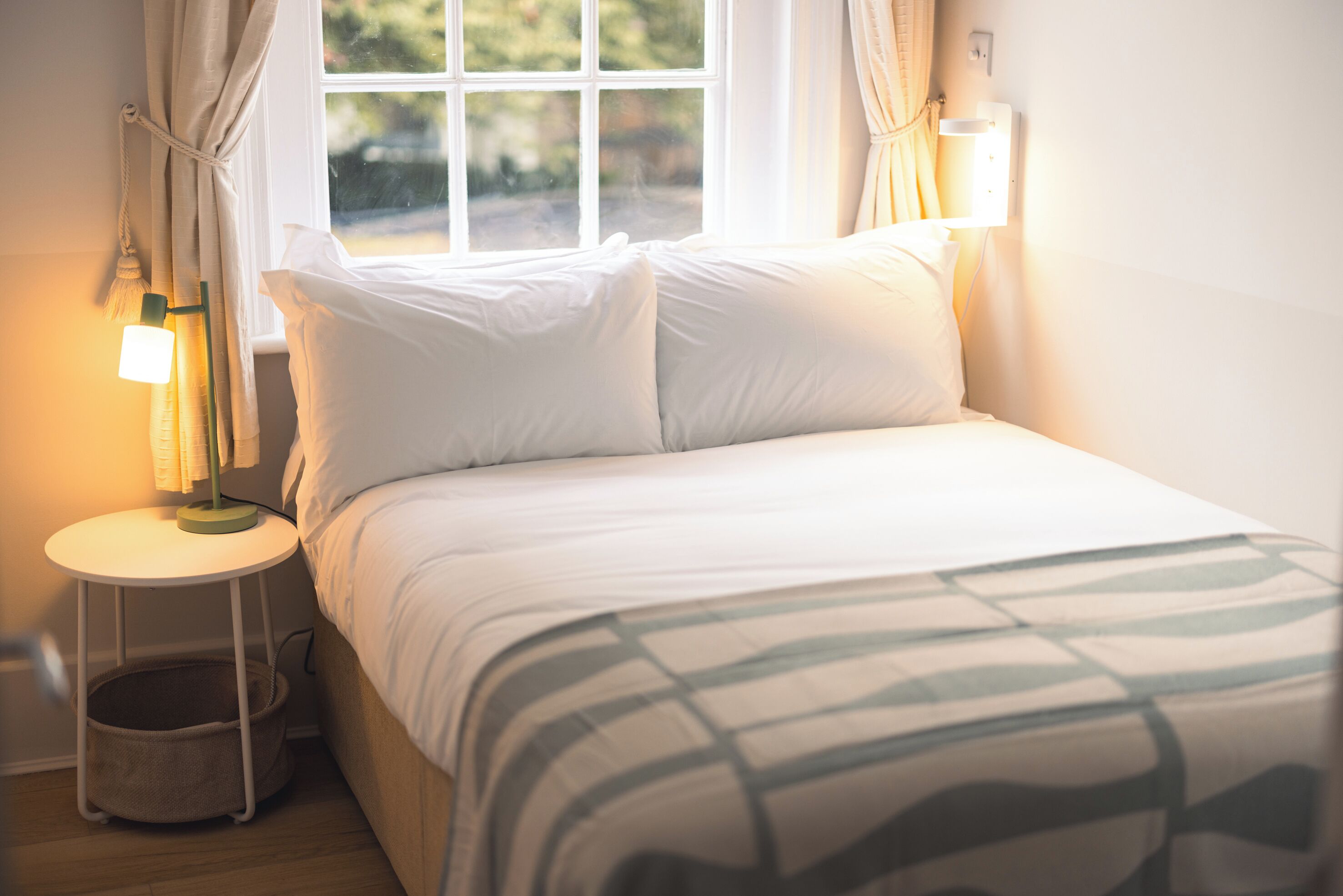 A neatly made bed with white bedding, a bedside lamp, and a small bedside table with a lamp.