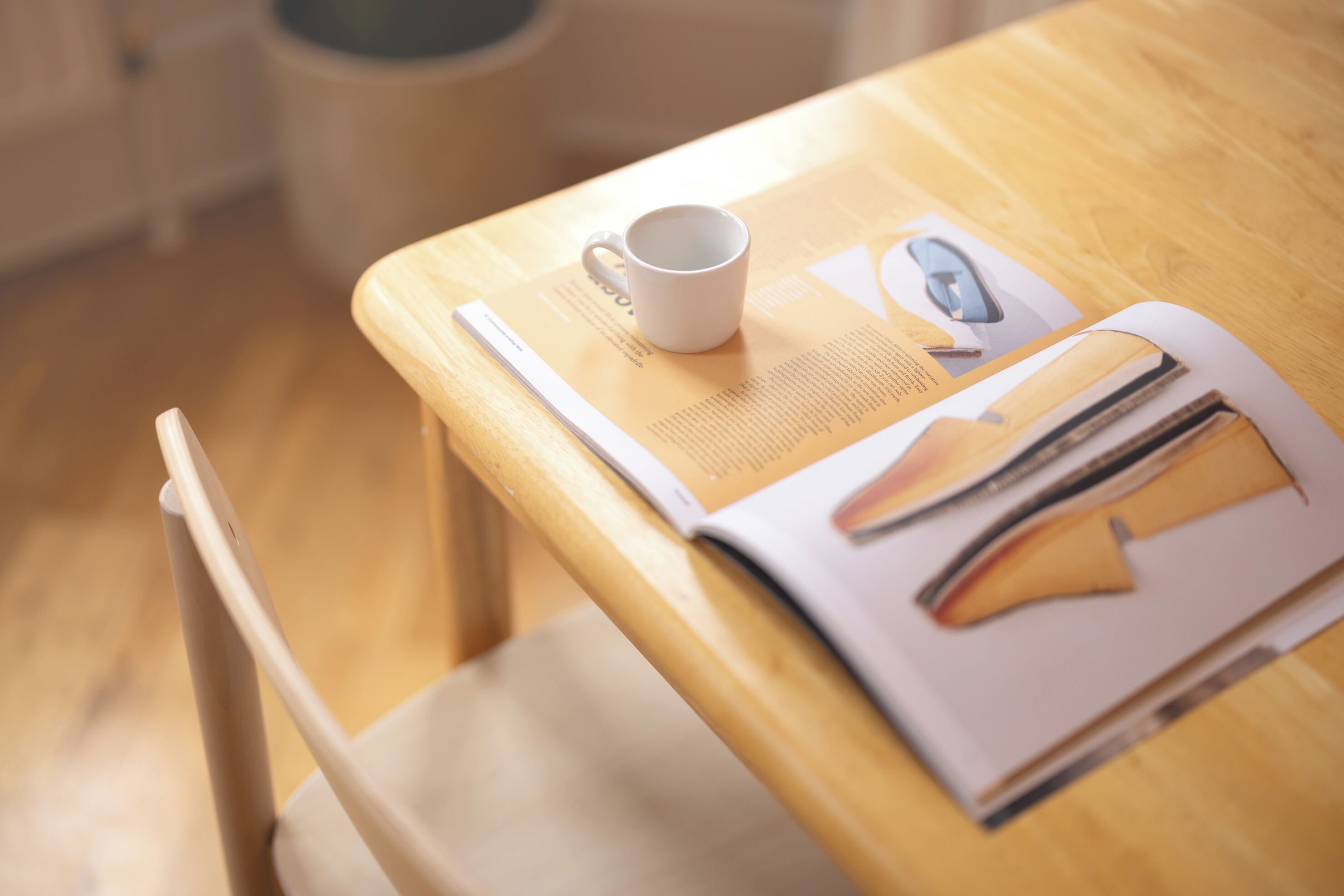 Une table en bois, sur laquelle se trouvent une tasse blanche, un magazine et une paire de ciseaux.