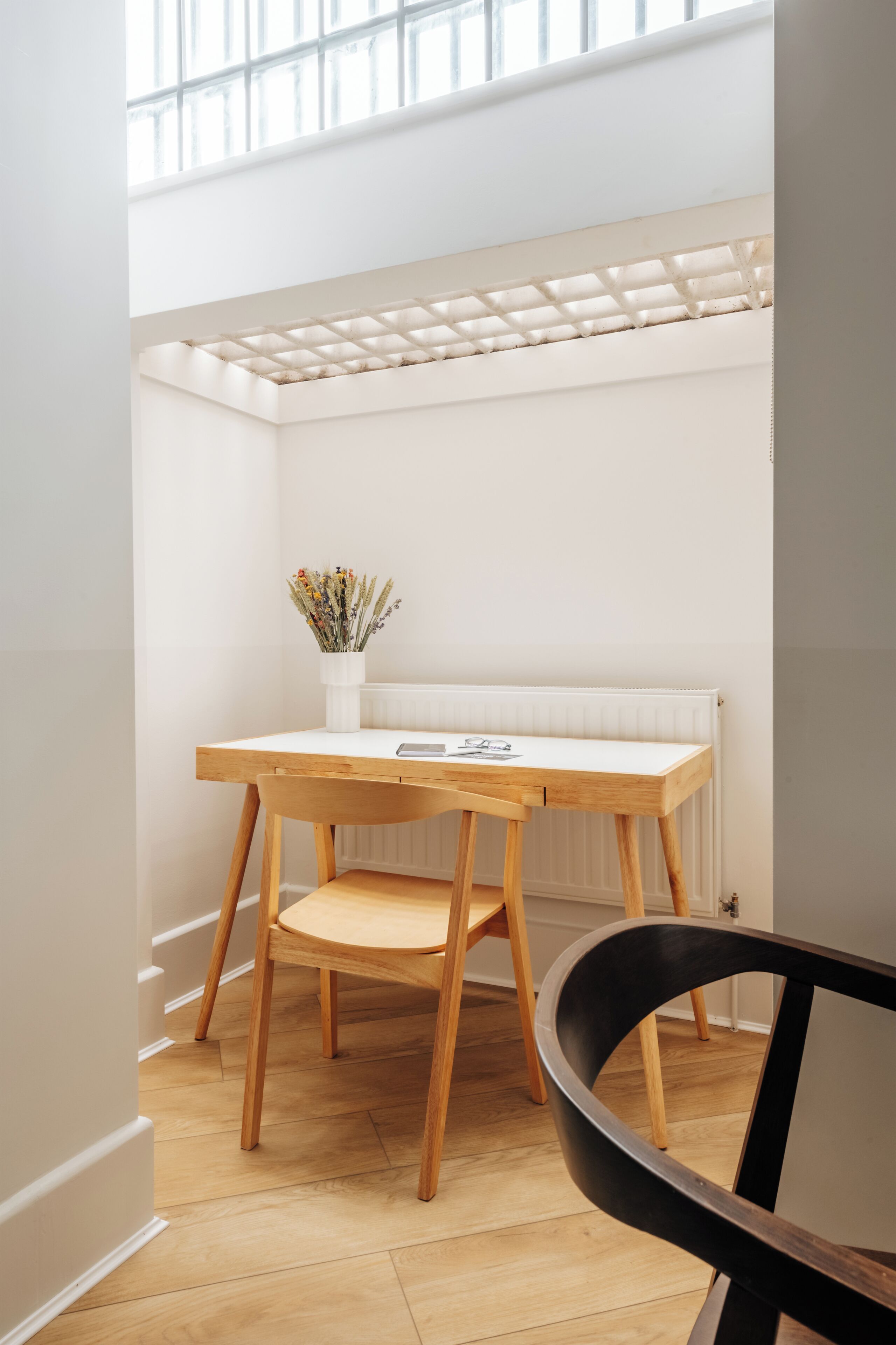 A small, bright room with a wooden desk and chair, a radiator, and a window with a grid pattern.