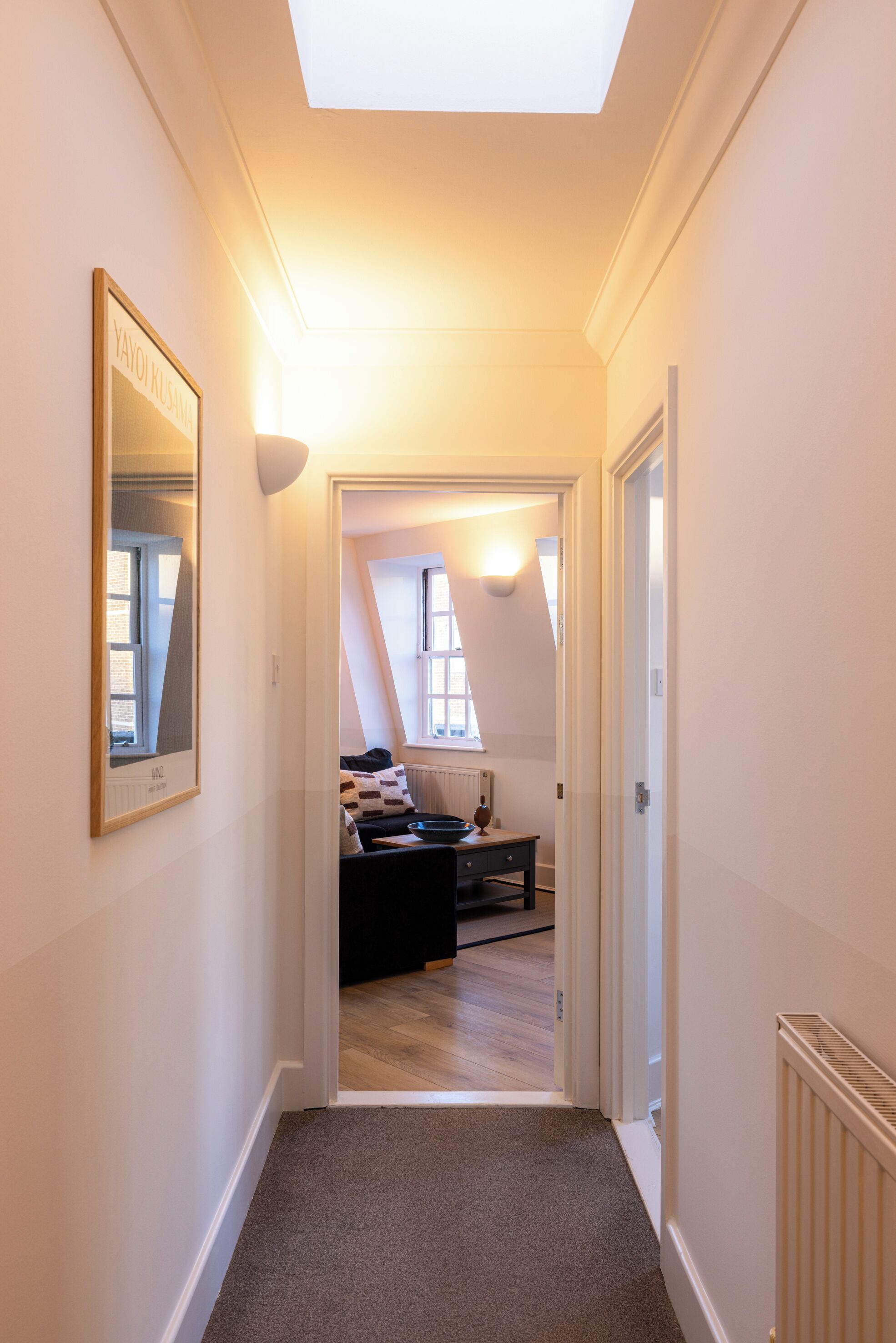 A narrow hallway with a skylight, leading to a bedroom with a bed and a radiator.
