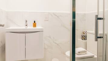 Une salle de bain moderne avec une douche à parois de verre, un lavabo blanc doté d’un plan de toilette en marbre et des toilettes agrémentées d’une serviette à carreaux.