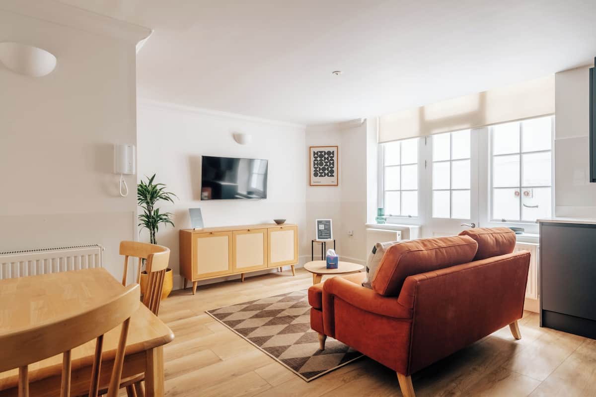 A modern living room with a wooden dining table, a red sofa, and a TV on the wall.