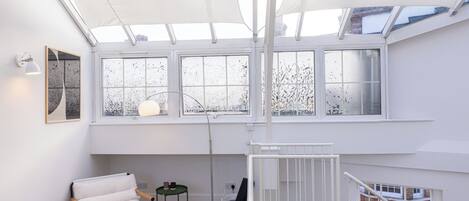 A spacious room with a high ceiling, a ceiling fan, a spiral staircase, and large windows providing natural light.