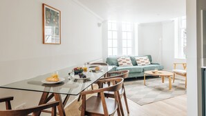 Ett modernt vardagsrum med ett matbord i glas, trästolar, en turkosfärgad soffa och ett soffbord.