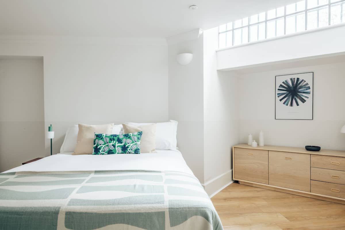 A modern bedroom with a bed, a wooden dresser, and a large window.