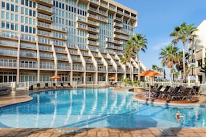 Un hotel con una piscina grande, varios balcones y palmeras.