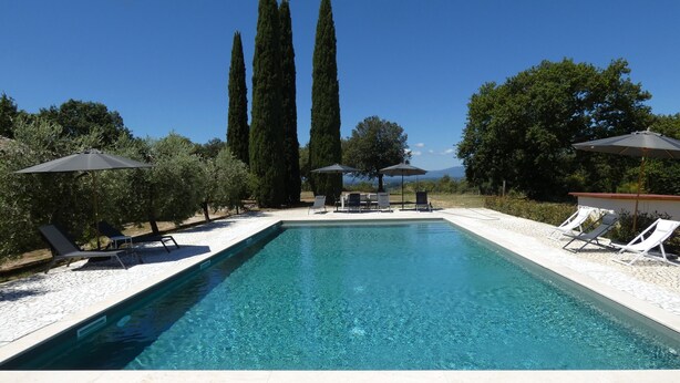A rectangular swimming pool with clear blue water, surrounded by white tiled deck and lounge chairs. Tall cypress trees are visible in the background. - SCAPPO IN UMBRIA, Casale Fasulo (Umbria)