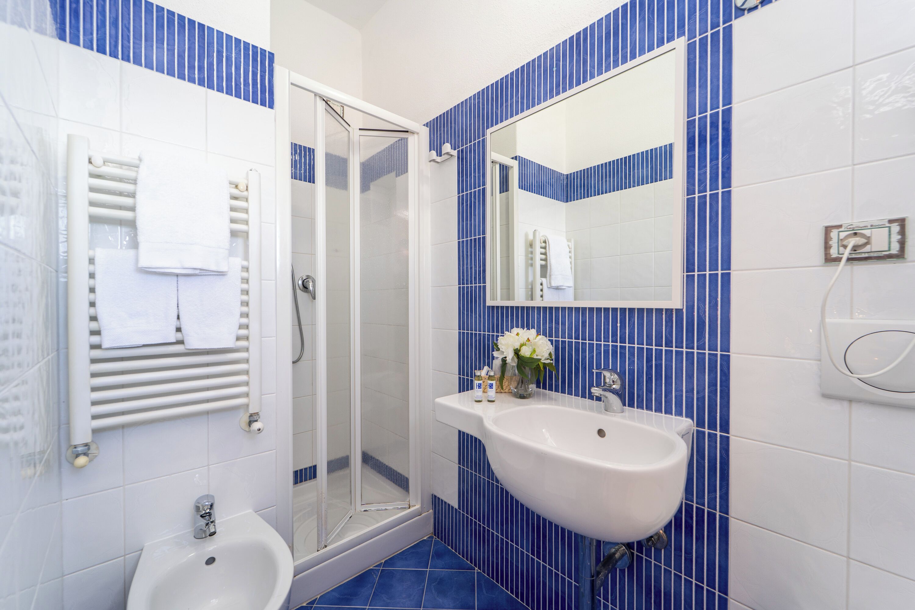 A bathroom with a white sink, a glass-enclosed shower, and blue-tiled walls.