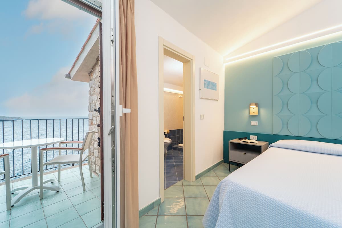 Et hotelværelse med balkon, seng, natbord og badeværelse, der kan ses igennem en åben dør.