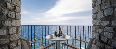 A balcony with a stone wall, a round table with two chairs, and a view of the ocean.