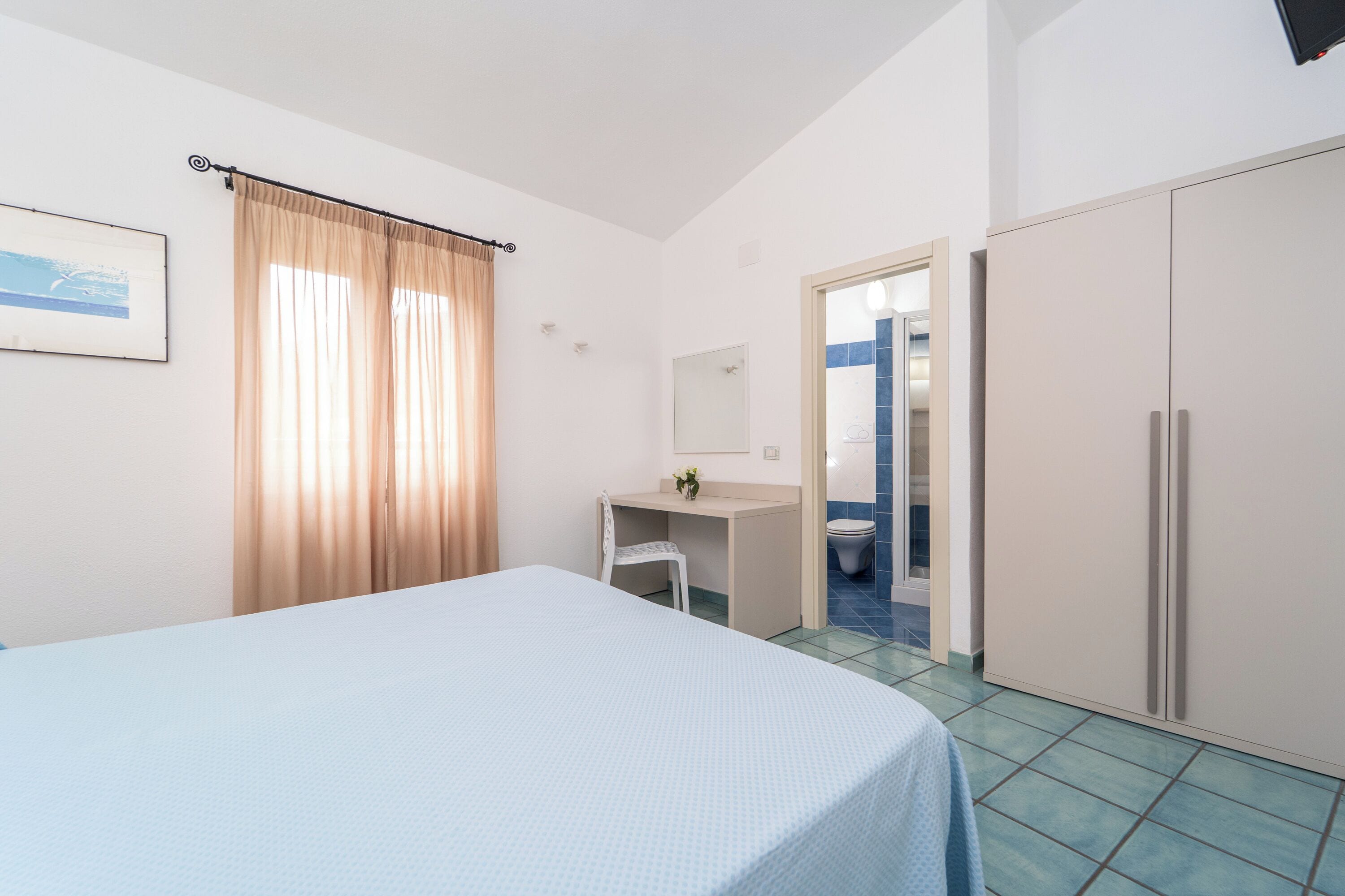 A bedroom with a bed, a desk, a chair, a wardrobe, and a bathroom visible through an open door.