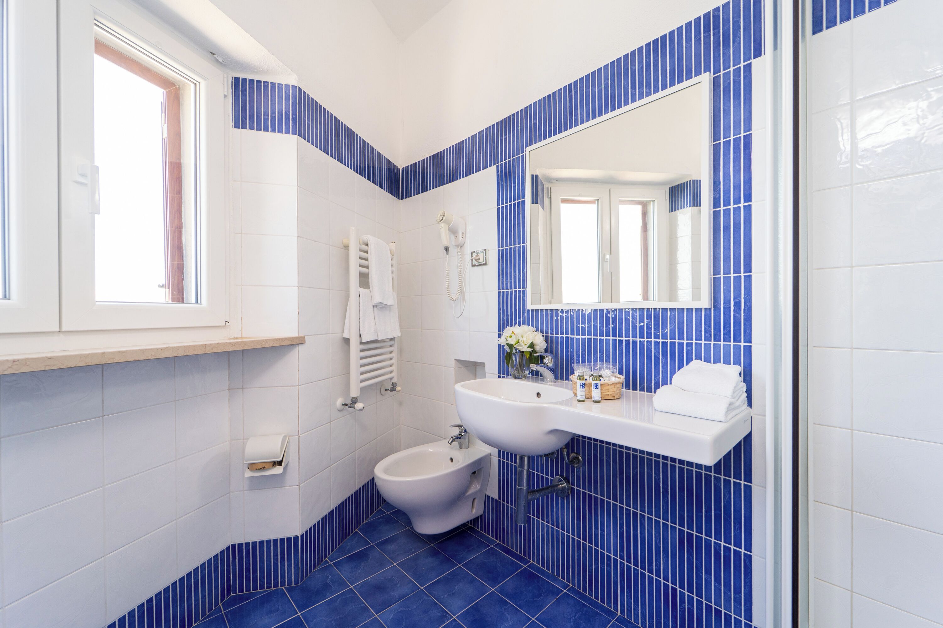 A bathroom with a bidet, a sink, a mirror, and a window.