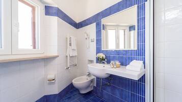 A bathroom with a bidet, a sink, a mirror, and a window.