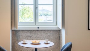 Ein kleiner runder Tisch mit zwei Tassen und einem Teller mit Muffins, platziert unter einem Fenster mit Blick auf Grünflächen und Hügel.