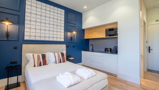 Ein modernes Hotelzimmer mit einem großen Bett, einer kleinen Küchenzeile und einer blauen Akzentwand.