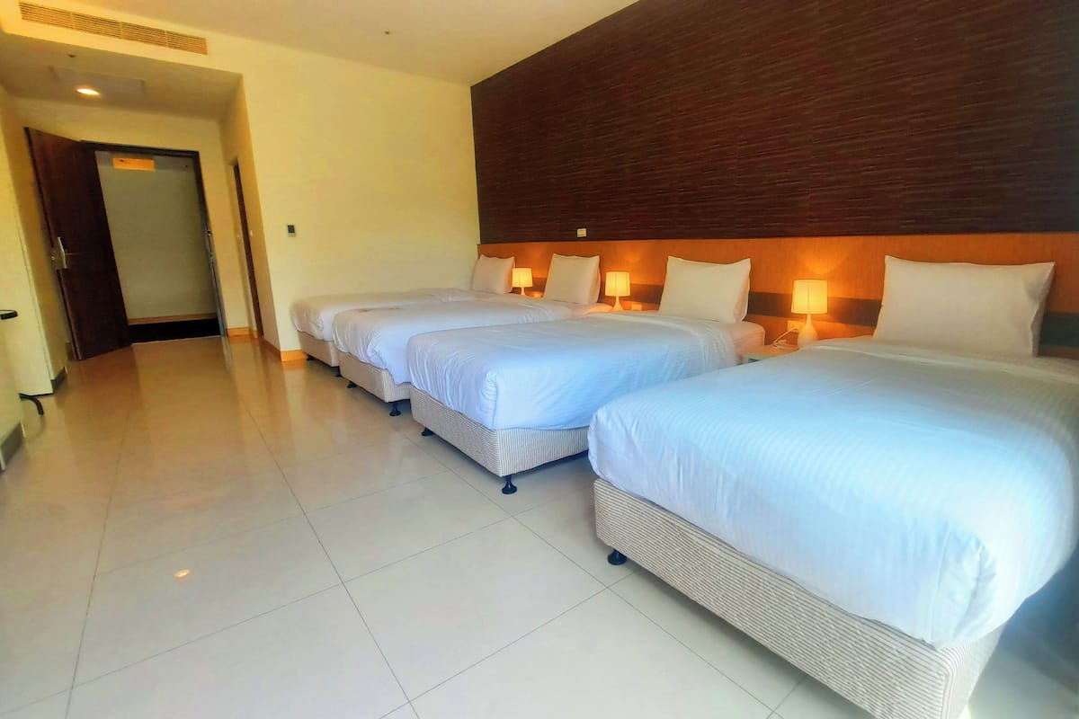 A hotel room with three single beds, a wooden headboard, bedside lamps, and a tiled floor.