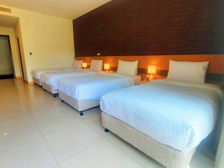 Una habitación de hotel con tres camas individuales, cabecera de madera, lámparas de noche y suelo de baldosas.