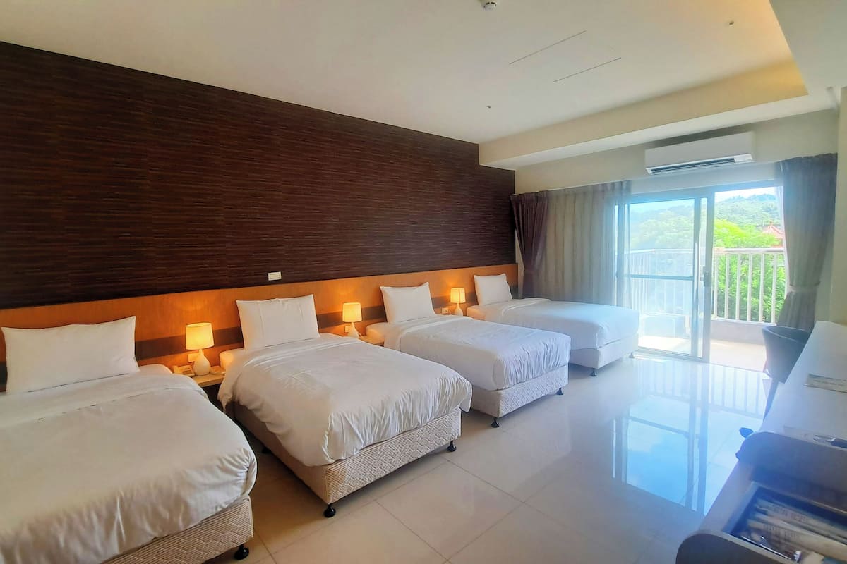 A hotel room with three beds, a large window with a view, and a flat-screen TV.
