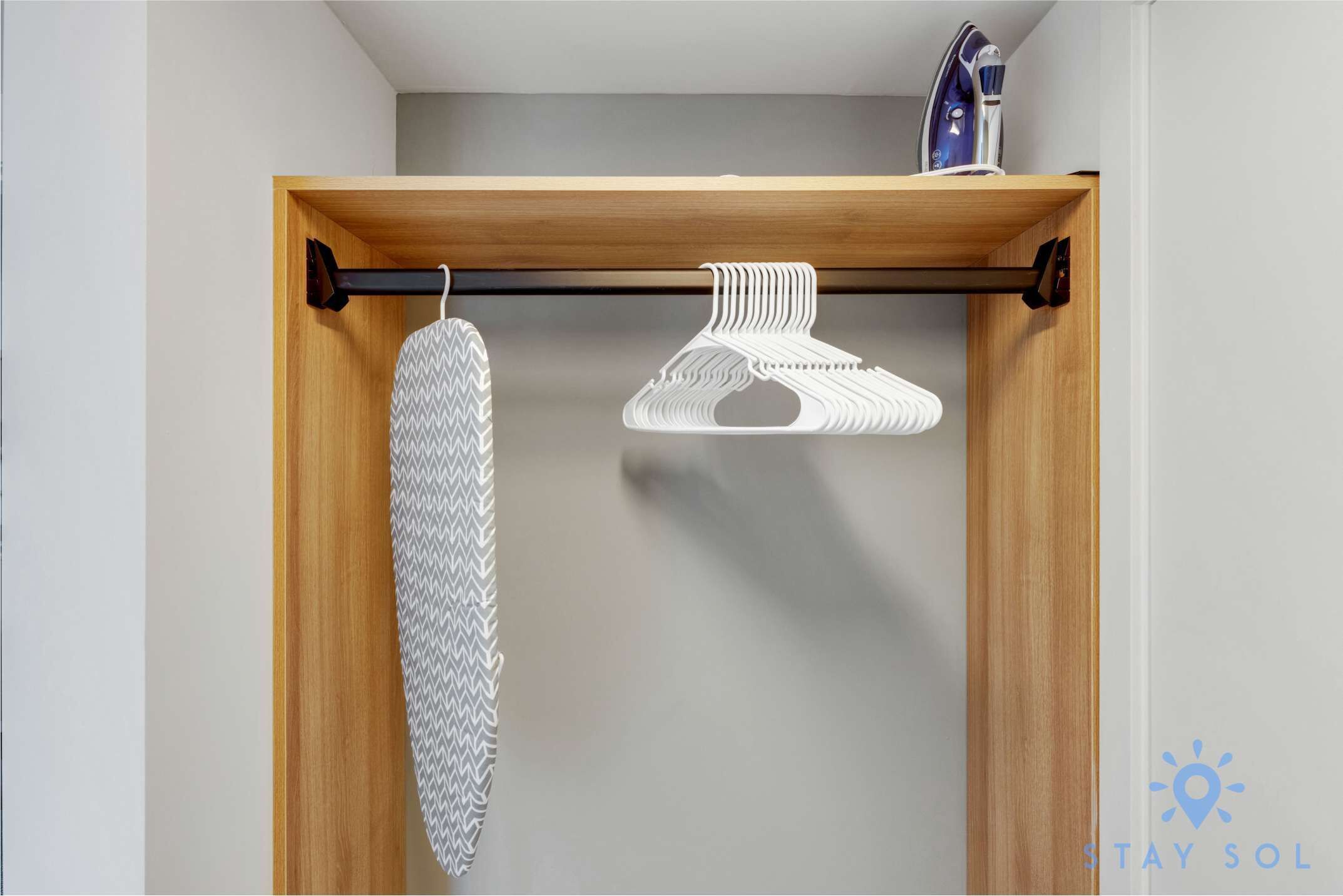 A wooden closet with a hanging rod, a white iron, and a patterned garment.