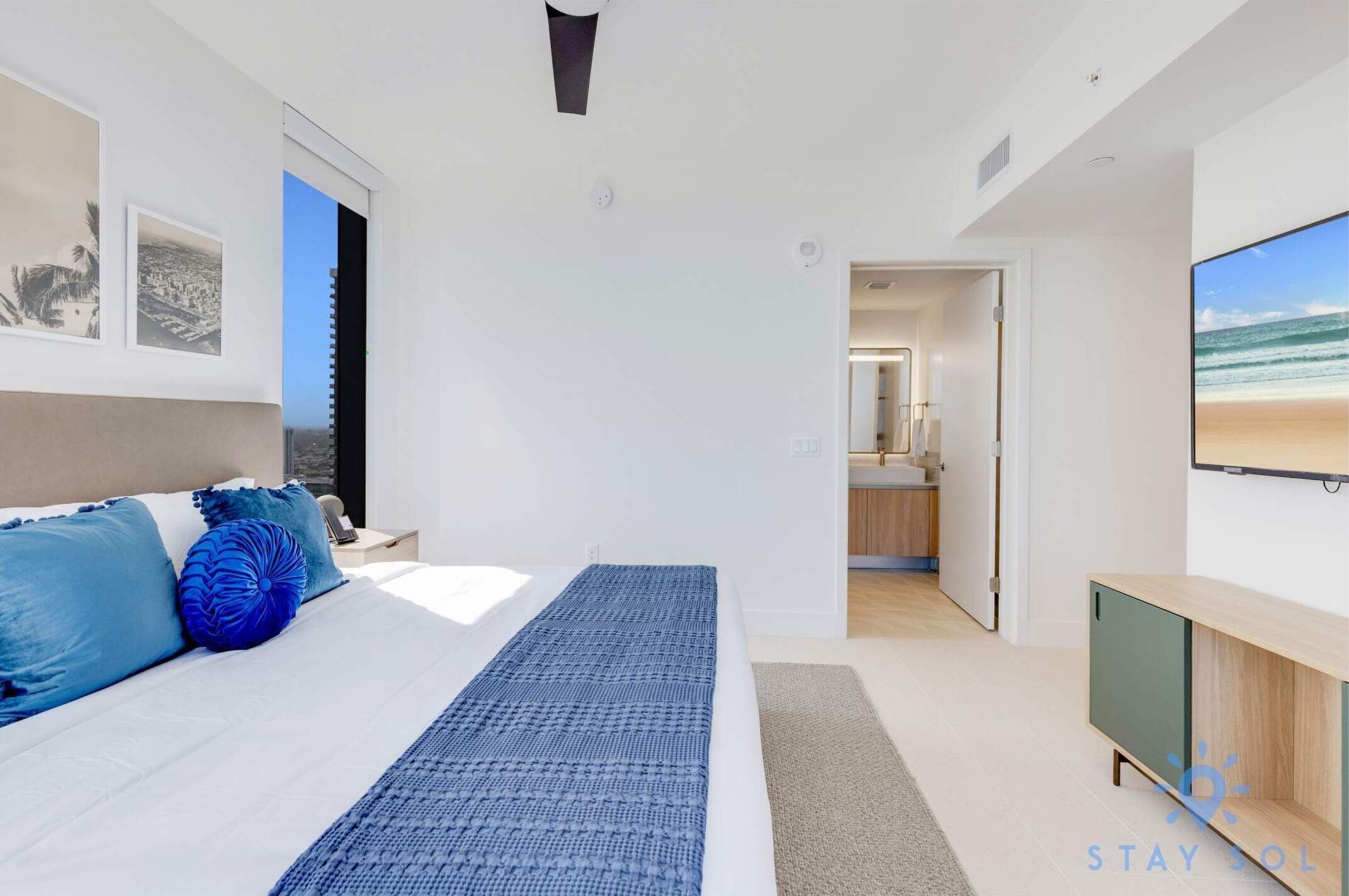 A modern bedroom with a large bed, a TV, and a view of the beach.