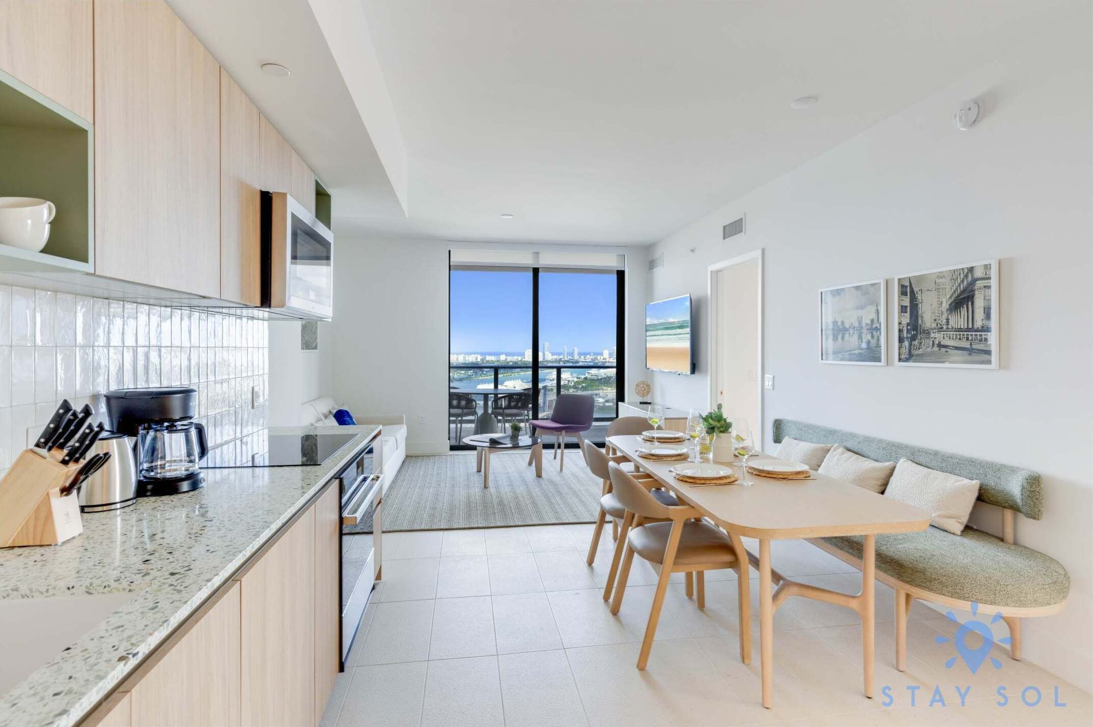 Een moderne keuken met een groot eiland, een eethoek met een bank, en een stadszicht door grote ramen.