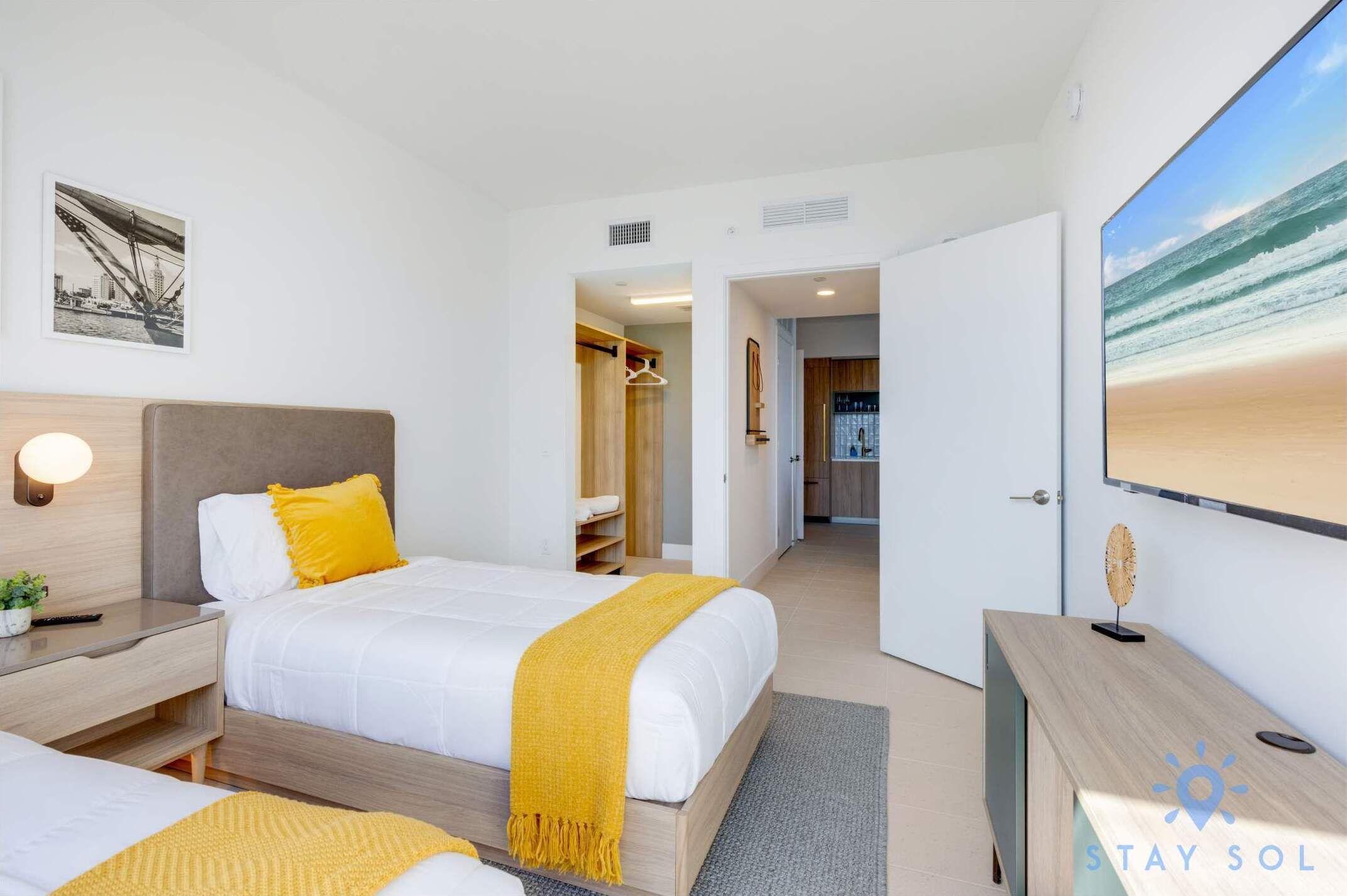 A modern hotel room with a large bed, bedside tables, a desk, and a large window with a beach view.