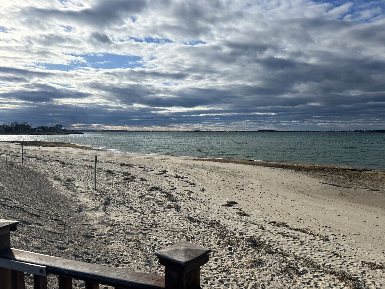 Ein Strand mit einem Holzzaun im Vordergrund und einem bewölkten Himmel.