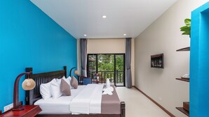 Camera d'albergo con un letto grande, un comodino in legno, una scrivania con una lampada, un balcone con vista sugli alberi e un piccolo ripiano con il telefono.