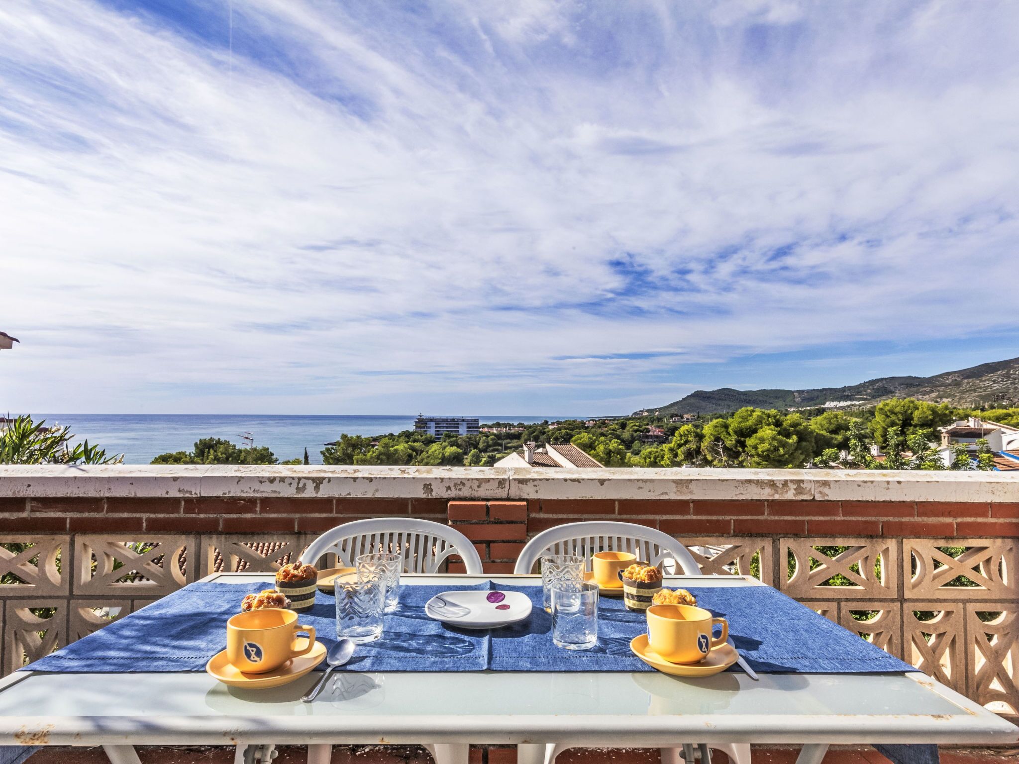 A table set for two with yellow cups and a plate, overlooking a coastal landscape.