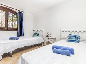 Ein Schlafzimmer mit zwei Einzelbetten, einem Nachttisch mit Lampe, einem Fenster mit Vorhängen und Blick auf Bäume.