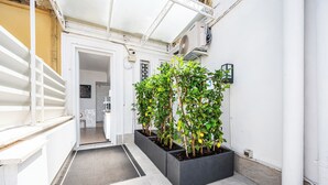 A narrow hallway with a white staircase on the left, a door at the end, and a row of potted lemon trees on the right. - Colonna Inn (Rome)