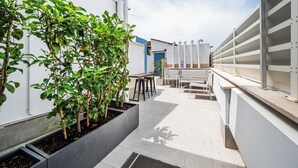 A rooftop patio with a seating area, planters with green plants, and a white railing. - Colonna Inn (Rome)