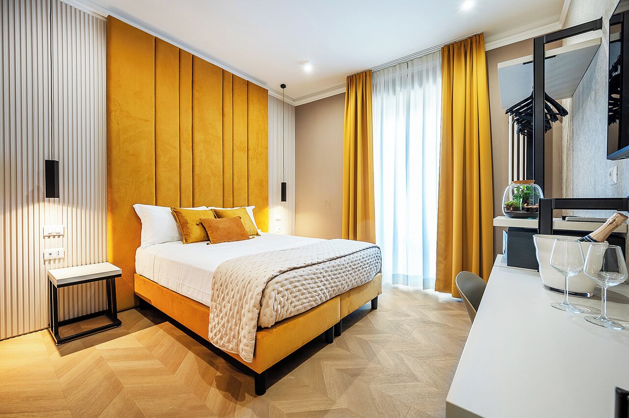 Une chambre d’hôtel moderne avec un grand lit, une table de chevet, un bureau avec deux verres et un miroir.