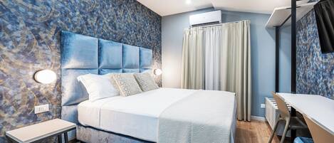 Un dormitorio moderno con una cama grande, mesitas de noche, un escritorio y un aire acondicionado.