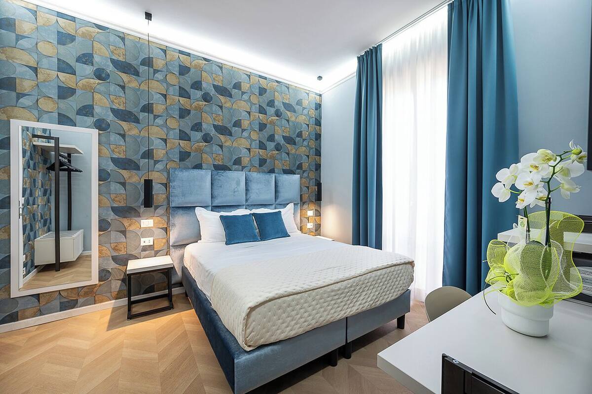A modern bedroom with a large bed, a bedside table, a mirror, a nightstand, and a vase with flowers.