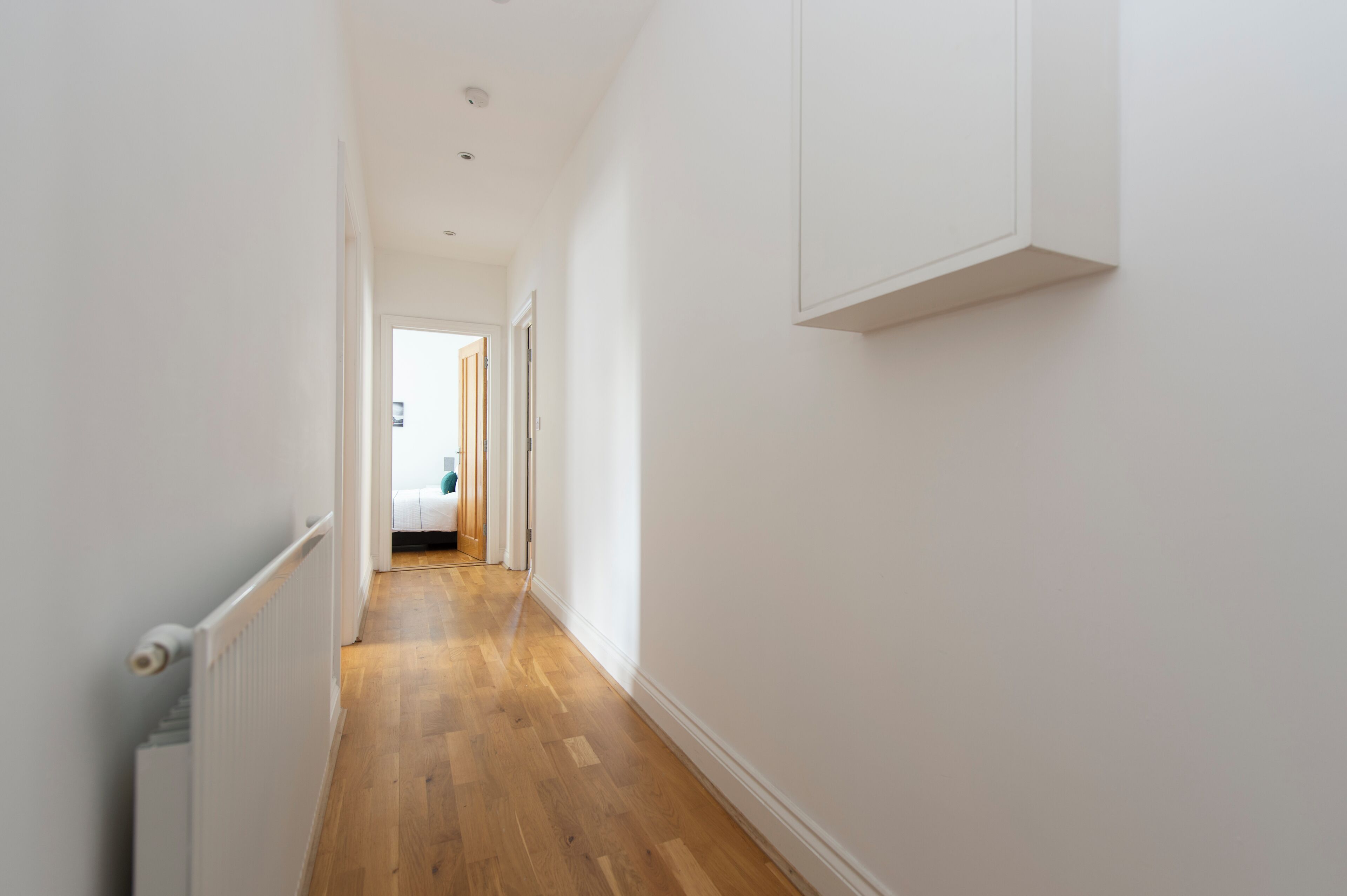 A narrow hallway with wooden flooring and white walls.