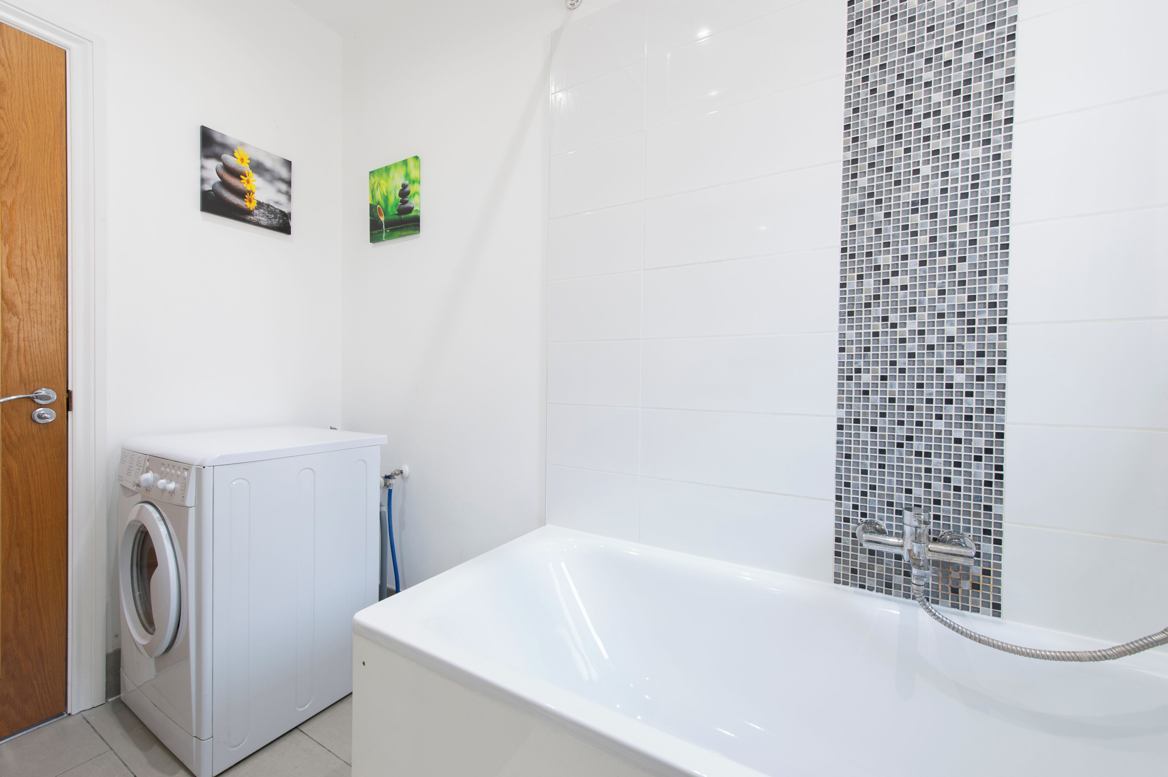 A bathroom with a white bathtub, a washing machine, and a tiled shower area.