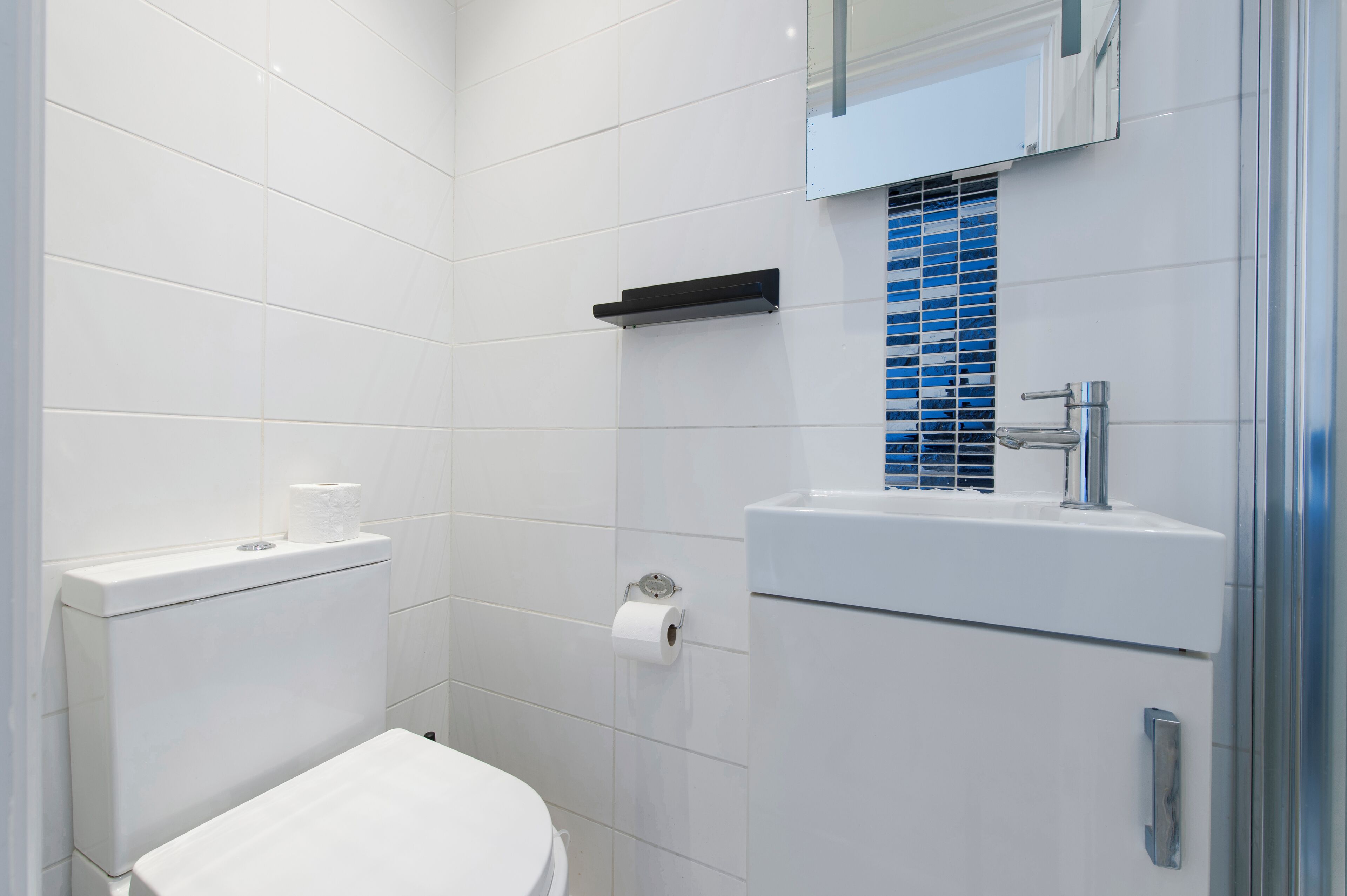 A modern bathroom with white tiles, a toilet, a sink, and a mirror.