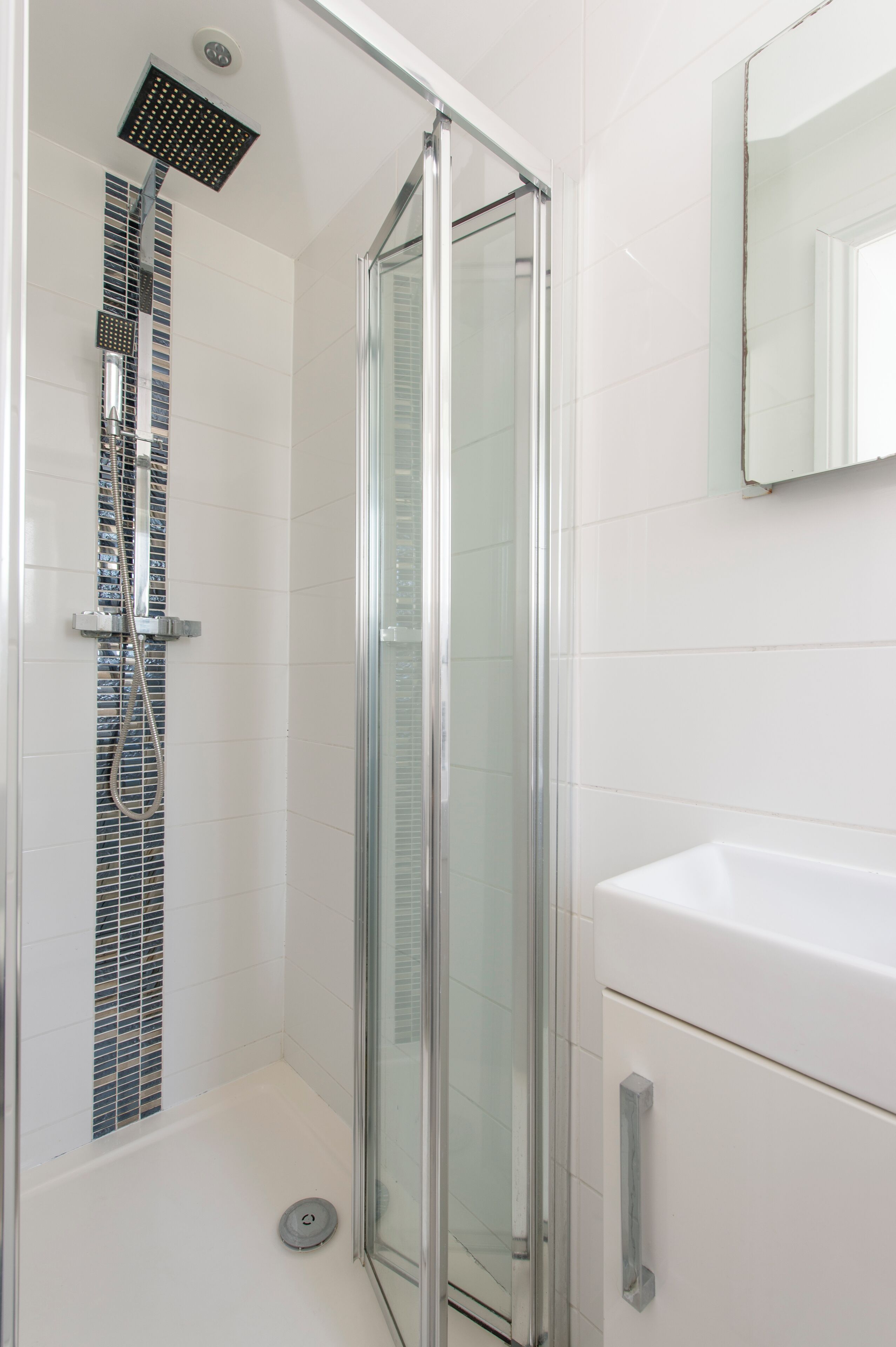 A modern bathroom with a glass-enclosed shower, a white sink, and a tiled wall.