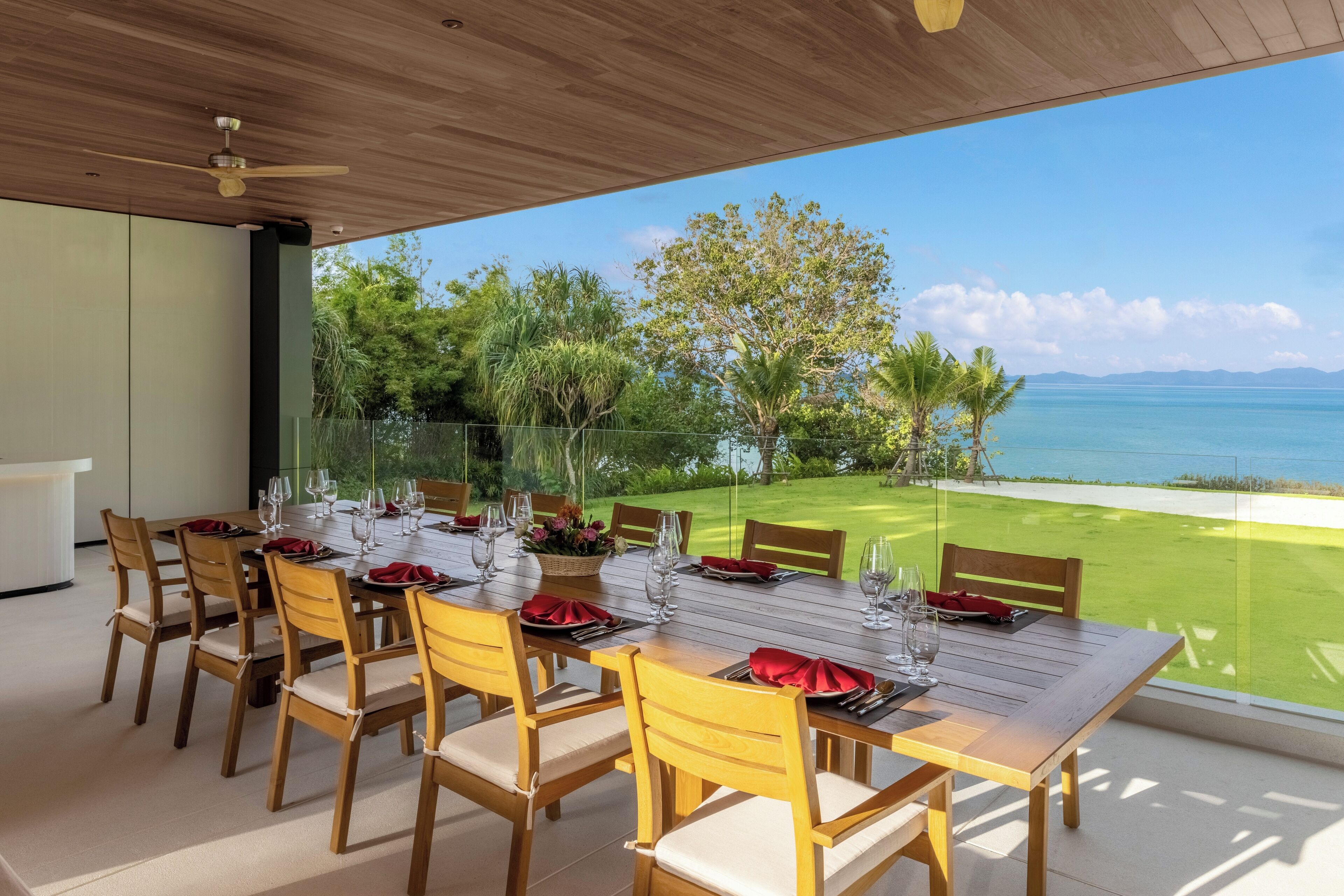 Comedor con mesa dispuesta para seis personas, con vistas a un jardín exuberante y al mar.