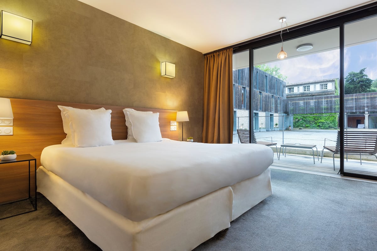 Una habitación de hotel moderna con una cama grande, lámparas de noche y vistas a un patio.