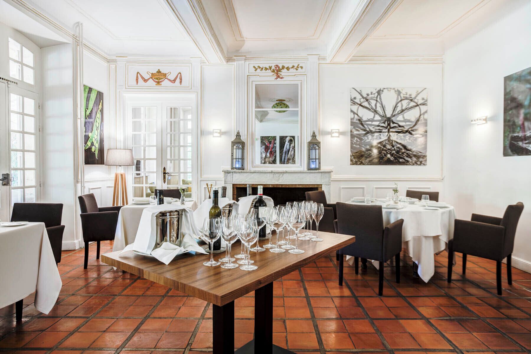 A dining area with a long wooden table set for a meal, surrounded by chairs. There are multiple wine glasses and bottles on the table.