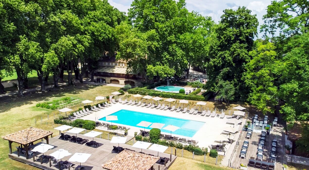 A pool area with lounge chairs and umbrellas, surrounded by trees and a parking lot.