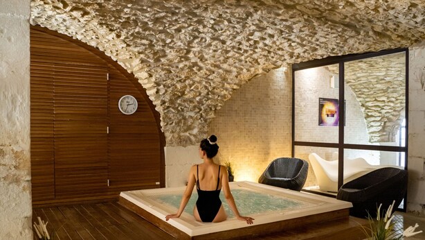Una stanza spa con soffitto in pietra, una porta in legno, un'ampia finestra e una vasca idromassaggio.
