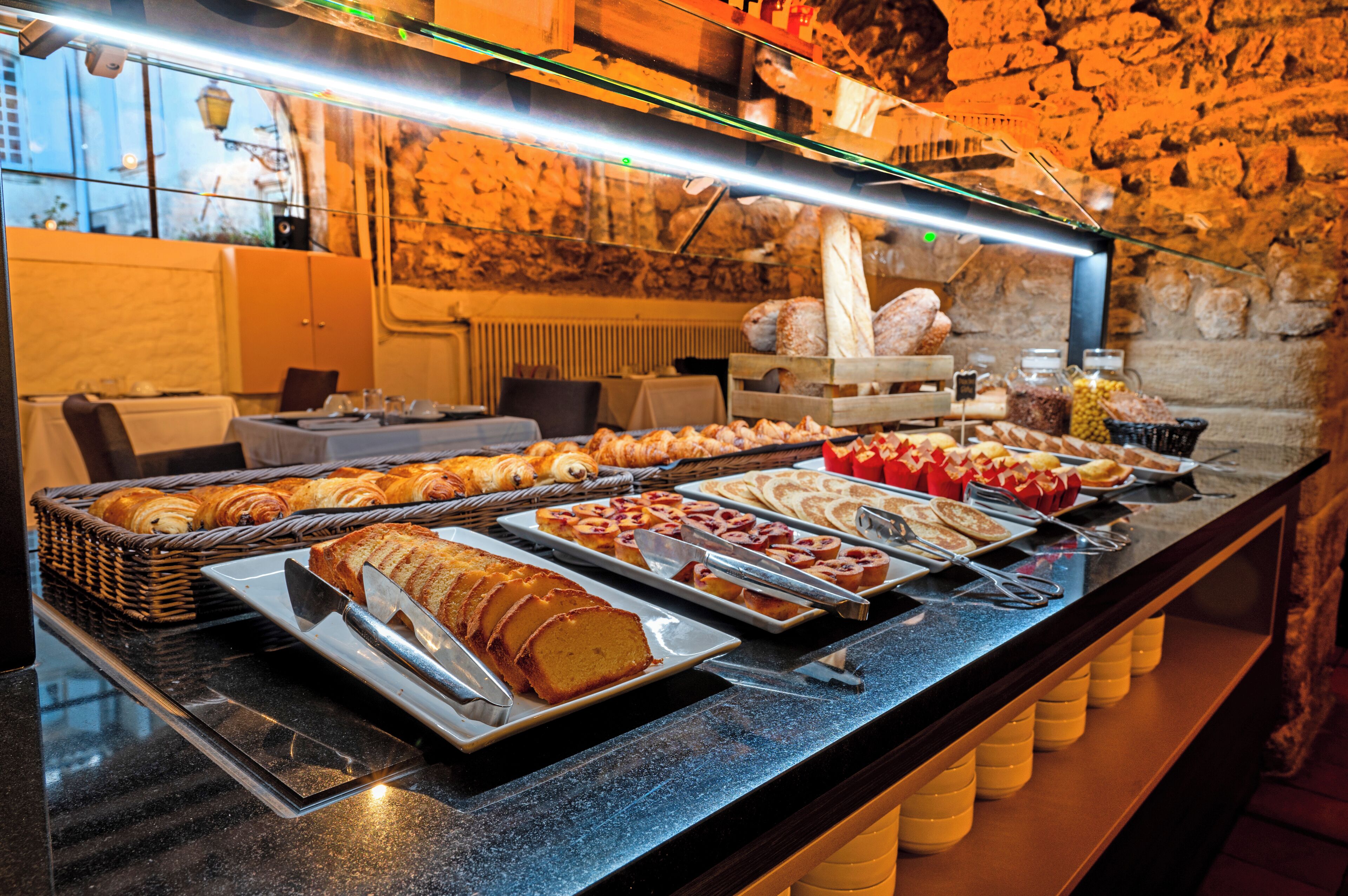 Un bufé con diversos alimentos, como pasteles y sándwiches, expuestos sobre una barra con un fondo de pared de piedra.