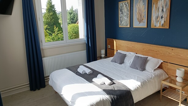 Ein Schlafzimmer mit einem Bett, einem Nachttisch, einem Fenster mit Vorhängen und zwei an der Wand befestigten Bildern.