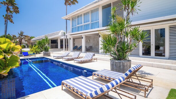 Un área de piscina moderna con sillones de descanso, una alberca y palmeras.