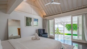 Un dormitorio espacioso con una cama grande, un ventilador de techo y vistas a un jardín exuberante a través de ventanas abiertas.