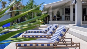 Zona junto a la piscina con sillones de descanso y un edificio moderno al fondo.